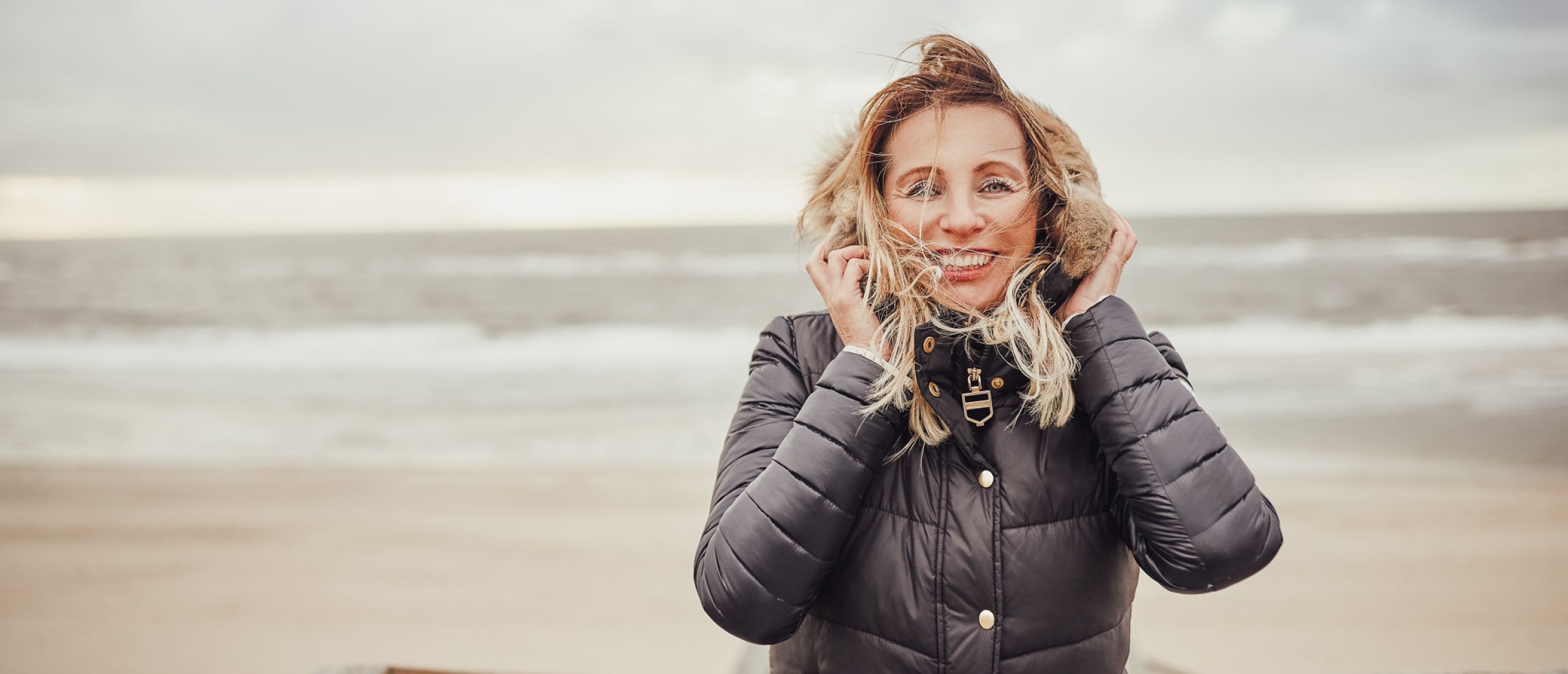 Eine Frau lächelt am Strand in Norddeich, während der Wind sanft durch ihr Haar weht.