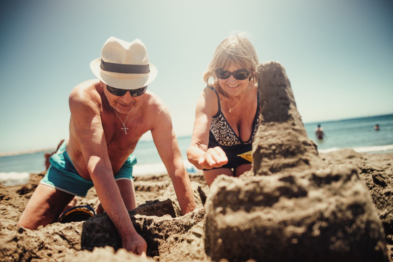 Ein älteres Paar baut gemeinsam eine Sandburg am Strand unter der Sonne.